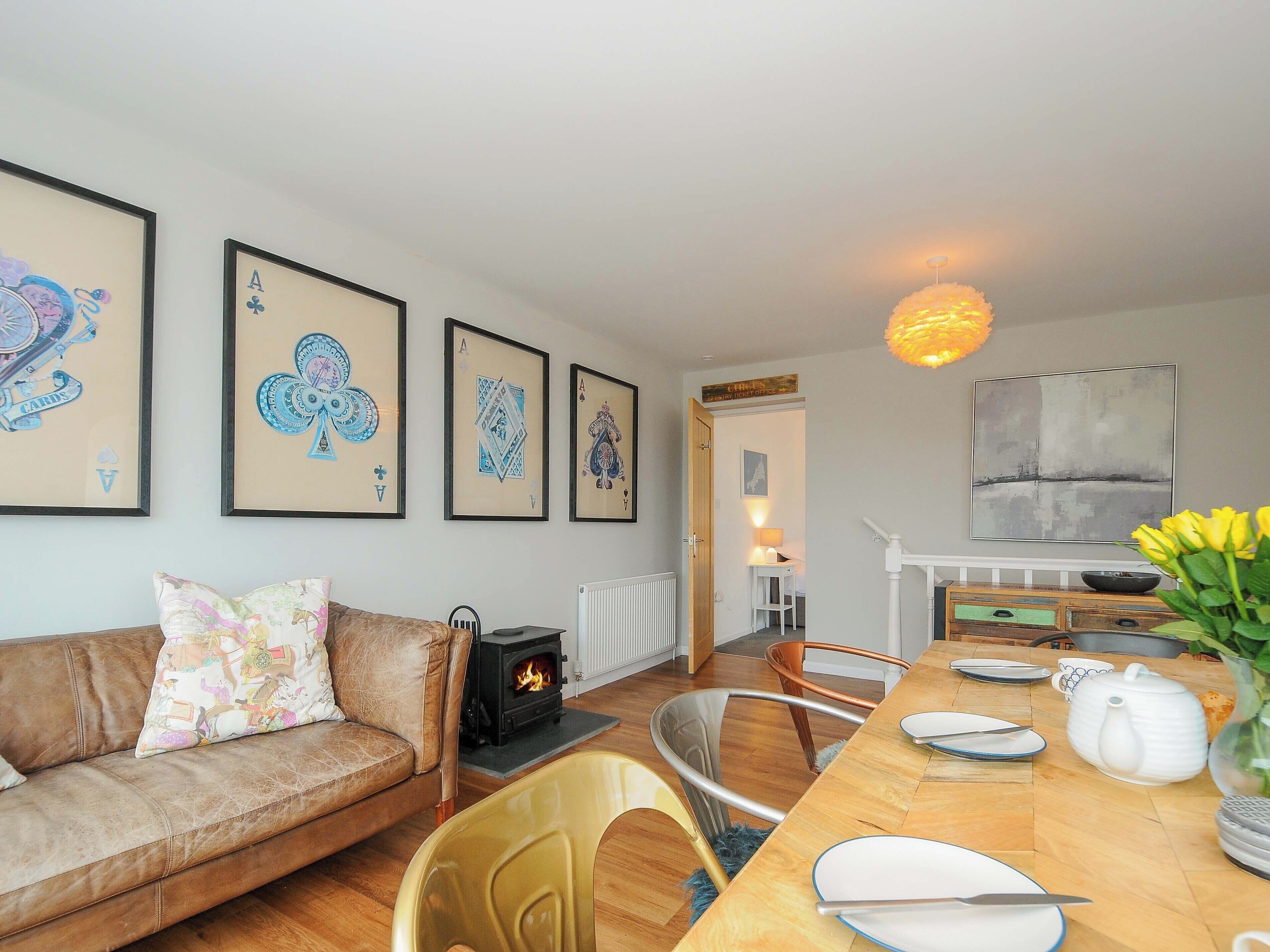 A cozy living room with a sofa, a dining table set with plates and a teapot, a fireplace, and framed artwork on the wall.