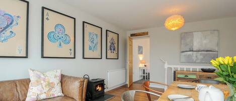 A cozy living room with a sofa, a dining table set with plates and a teapot, a fireplace, and framed artwork on the wall.