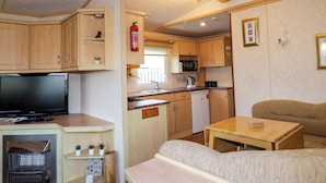 A compact RV kitchen with wooden cabinets, a microwave, a sink, and a small dining area. - Meric Stone Holiday Lets Caravan 2 (Limavady)