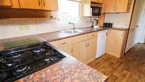 A kitchen with granite countertops, wooden cabinets, a stove, a microwave, and a dishwasher. - Meric Stone Holiday Lets Caravan 2 (Limavady)