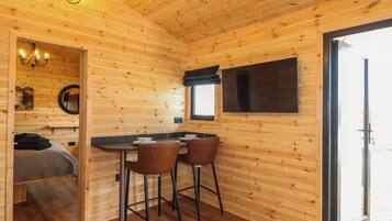 Ein Interieur einer Holzhütte mit Essbereich, einem Bett und einem an der Wand montierten Fernseher.