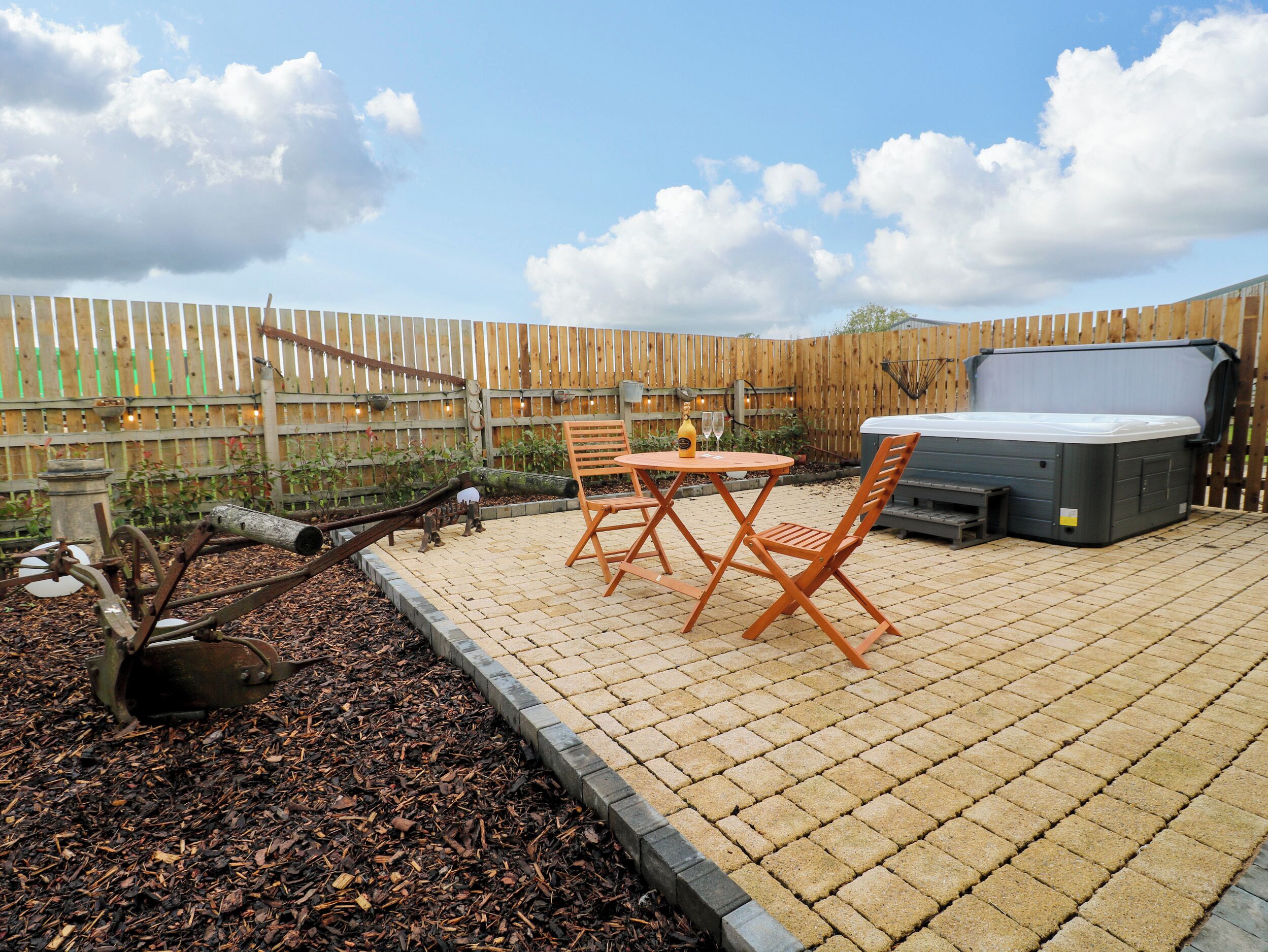 A patio with a hot tub, wooden chairs, and a table.