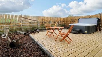 A patio with a hot tub, wooden chairs, and a table.