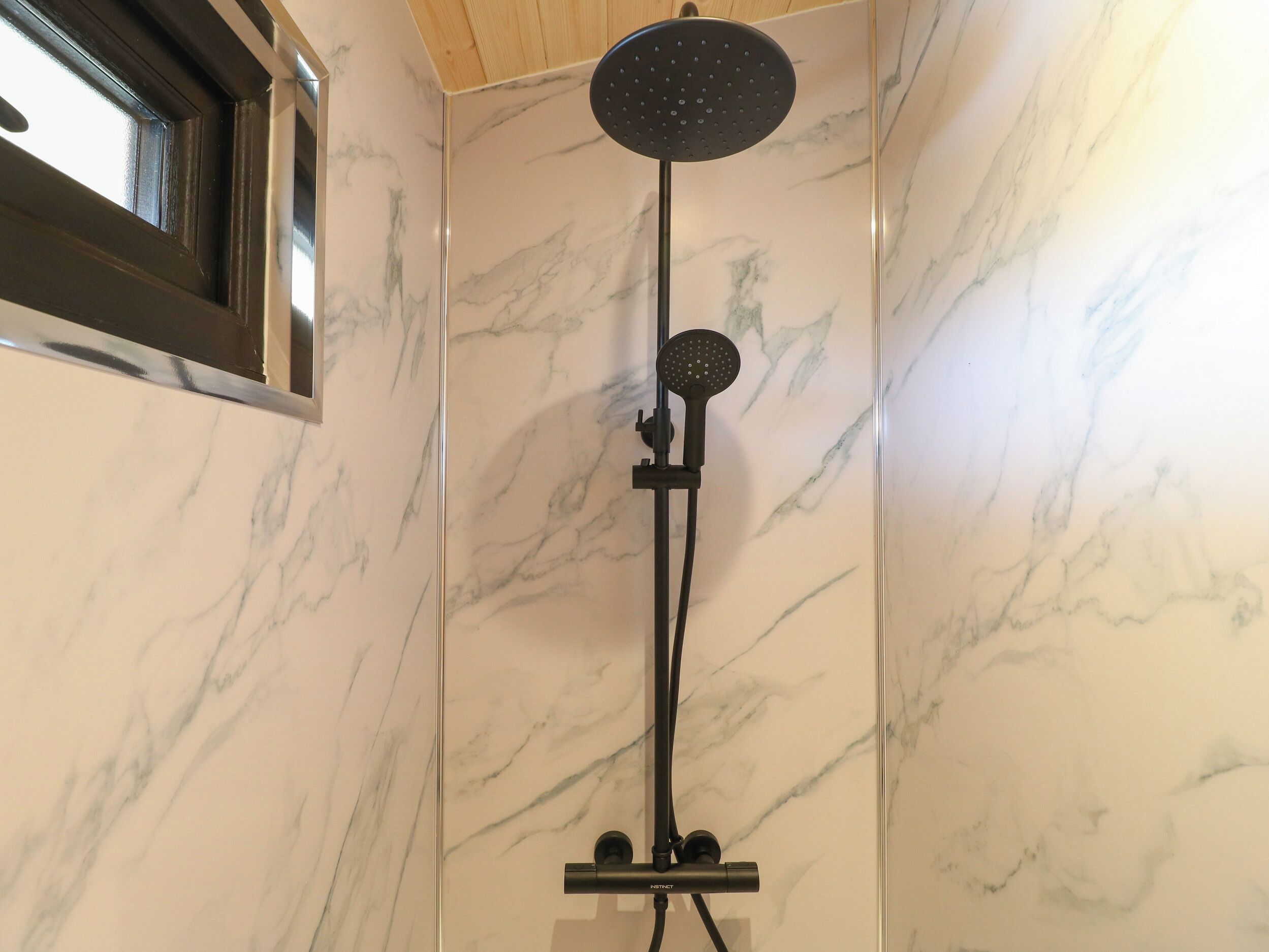 Une douche équipée d’un pommeau de douche à main et d’une douchette à pluie fixée au mur, le tout sur un mur recouvert de carreaux de marbre.