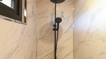 Une douche équipée d’un pommeau de douche à main et d’une douchette à pluie fixée au mur, le tout sur un mur recouvert de carreaux de marbre.