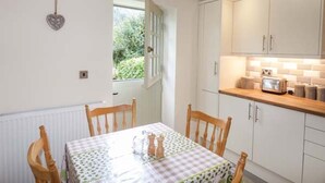 A dining area with a table set for four, wooden chairs, and a window with a view of greenery. - Beaver Grove Cottage (Betws-Y-Coed)