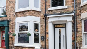 A townhouse with a white front door labeled "23 TRAF," a small outdoor seating area with a wooden table, and a brick facade. - 23 Trafalgar Square (Scarborough)