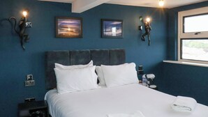 A hotel room with a large bed, two wall-mounted lights, a window with a view, and a nightstand with a phone and a lamp. - 23 Trafalgar Square (Scarborough)