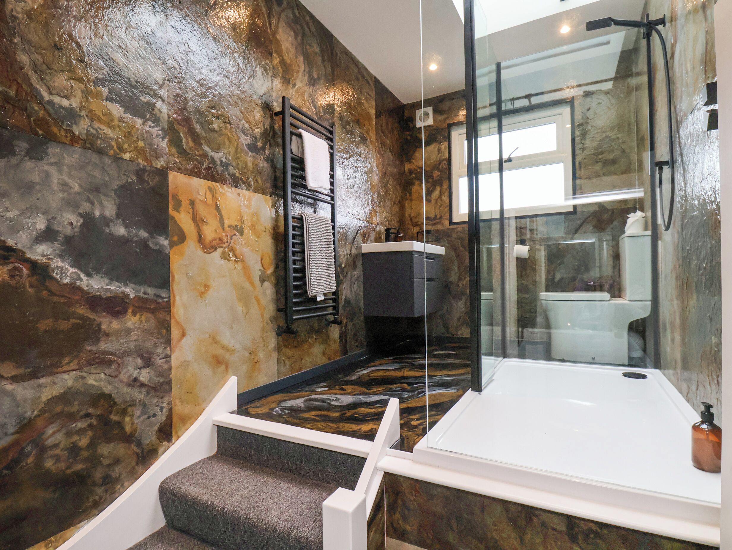 A modern bathroom with a stone wall, a glass shower enclosure, a white bathtub, and a towel rack.