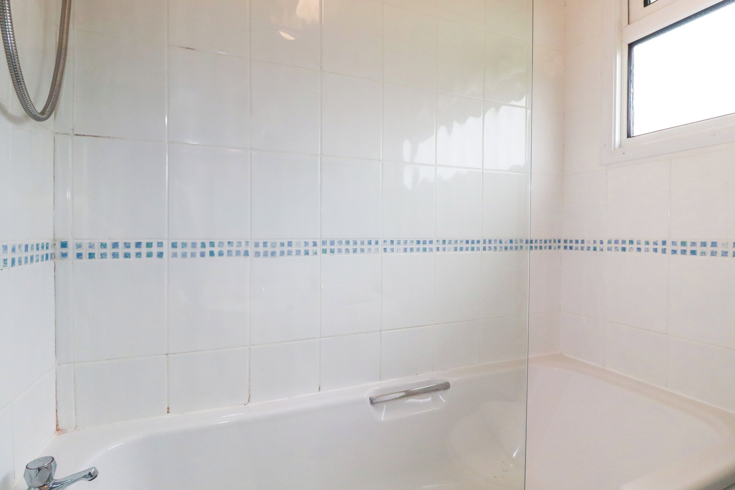 A bathroom with white tiled walls, a bathtub, and a shower hose.