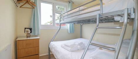 A bunk bed room with a wooden dresser and a window with curtains.