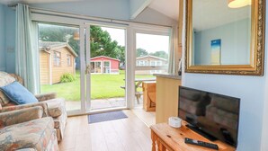 A living room with a sofa, a television on a wooden table, and a sliding glass door leading to a patio. - High Cove (Wadebridge)