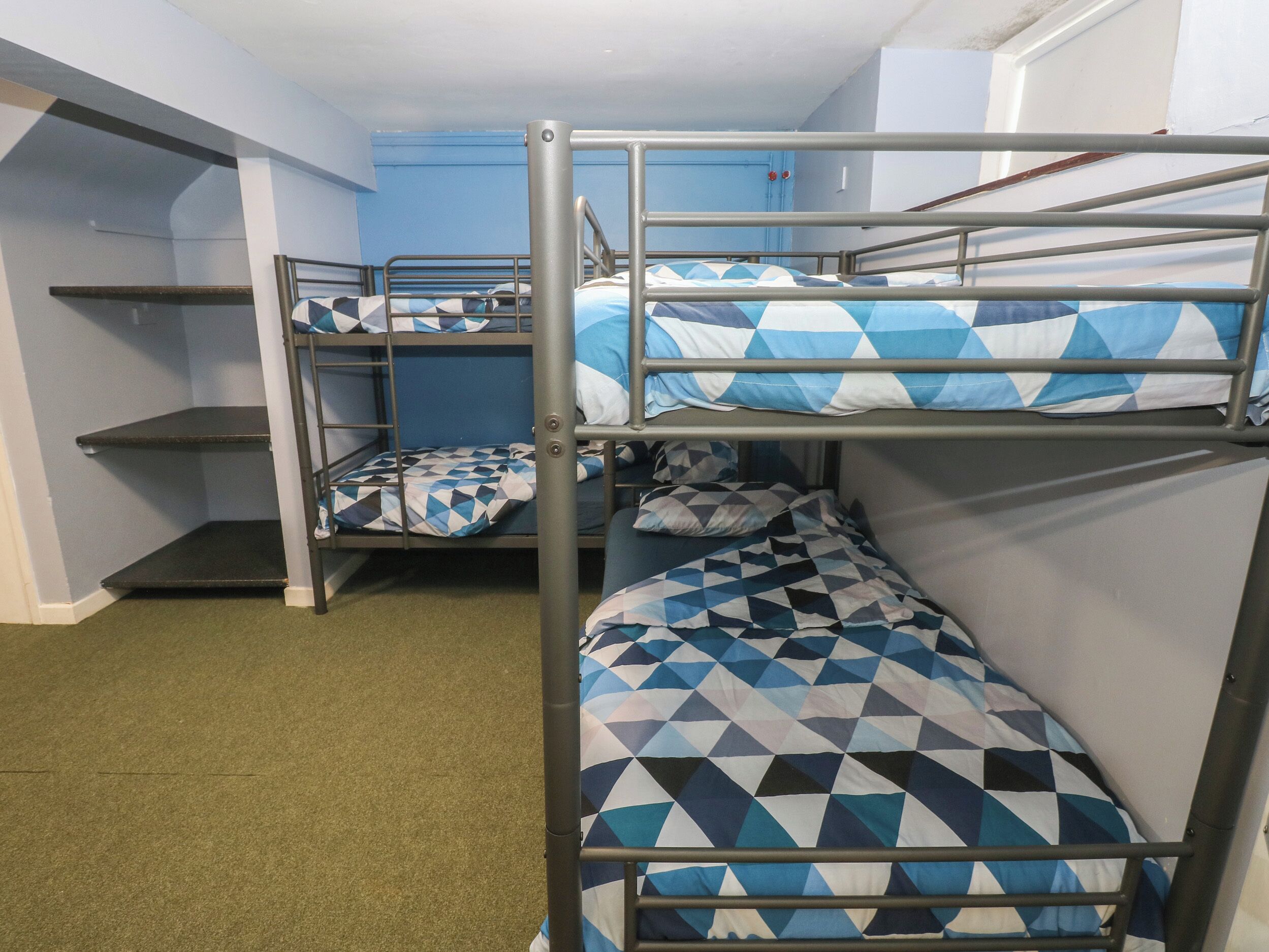 Une chambre de dortoir avec des lits superposés, une porte bleue et une moquette verte.