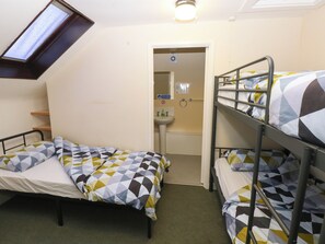 Une chambre de dortoir avec deux lits simples et un lit superposé, une lucarne, un lavabo et un miroir dans la salle de bain.