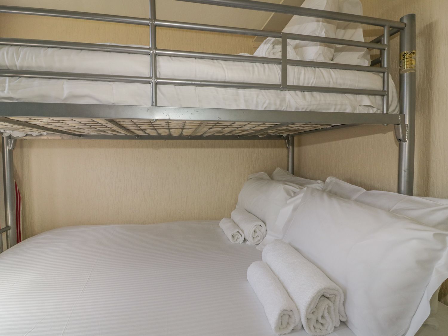A bunk bed with white bedding and rolled towels.
