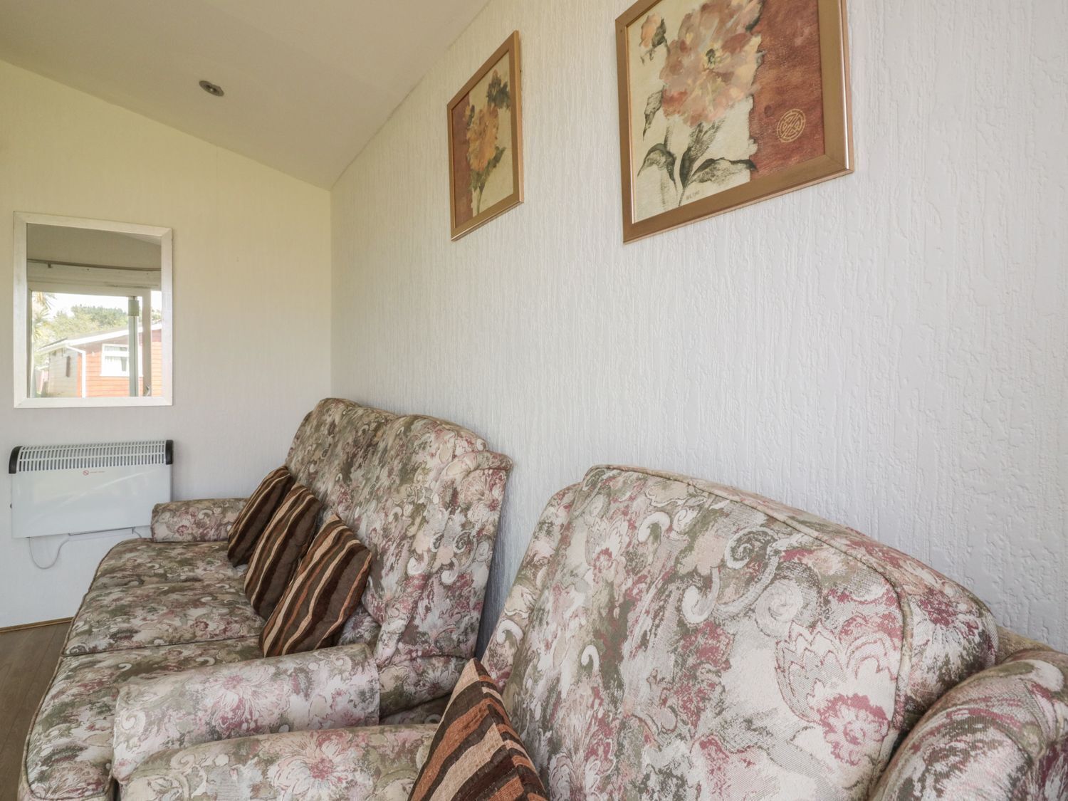 A living room with a floral-patterned sofa, two cushions, a radiator, and two framed floral paintings on the wall.