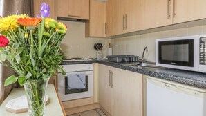 A kitchen with wooden cabinets, a microwave, a stove, and a sink. There is a vase with flowers on the counter. - Warren Cove (Wadebridge)