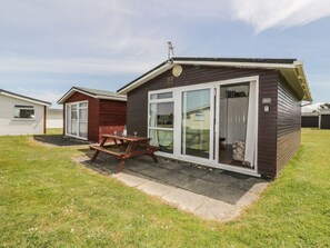 A small, single-story mobile home with a picnic table in front, a sliding glass door, and a number '157' on the door. - Warren Cove (Wadebridge)
