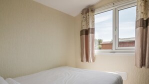 A bedroom with a bed, a window with curtains, and a radiator. - Warren Cove (Wadebridge)