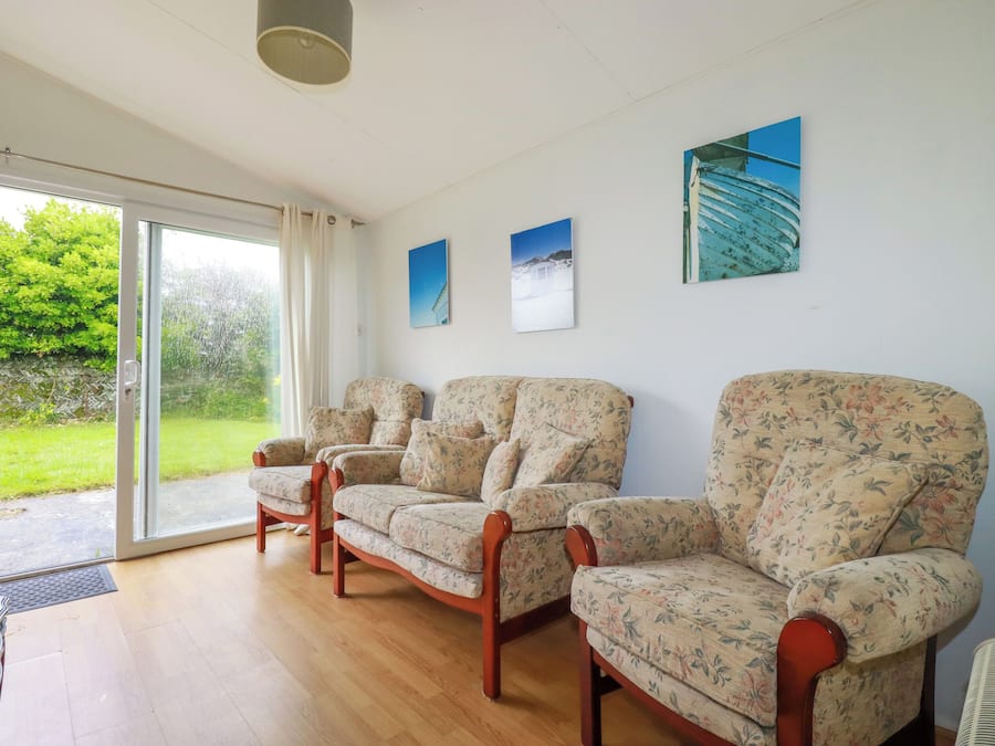 A room with three floral-patterned armchairs, a wooden floor, and a glass door leading to a garden.