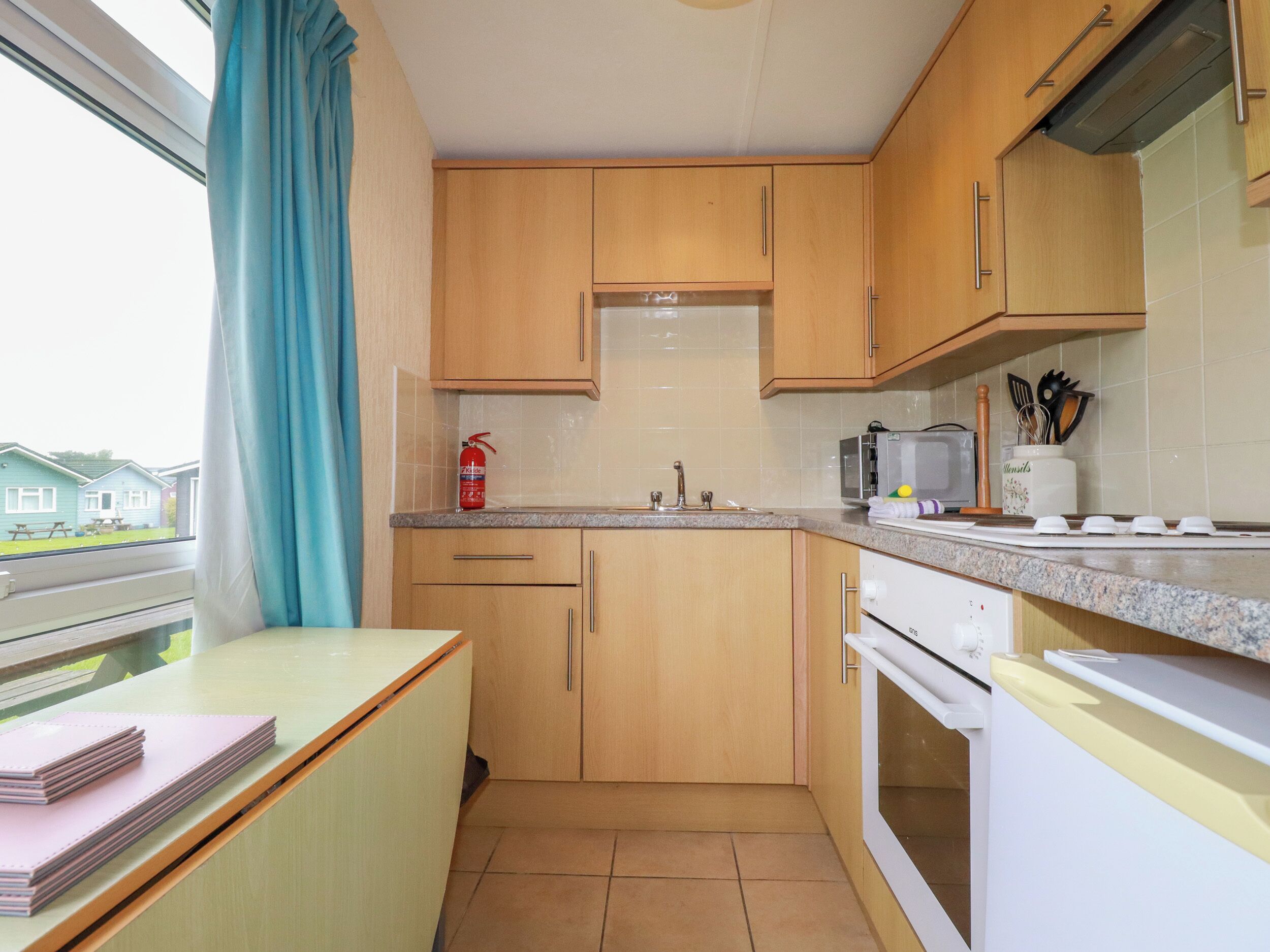 Una cocina compacta con armarios de madera, un microondas, una estufa y un extintor.