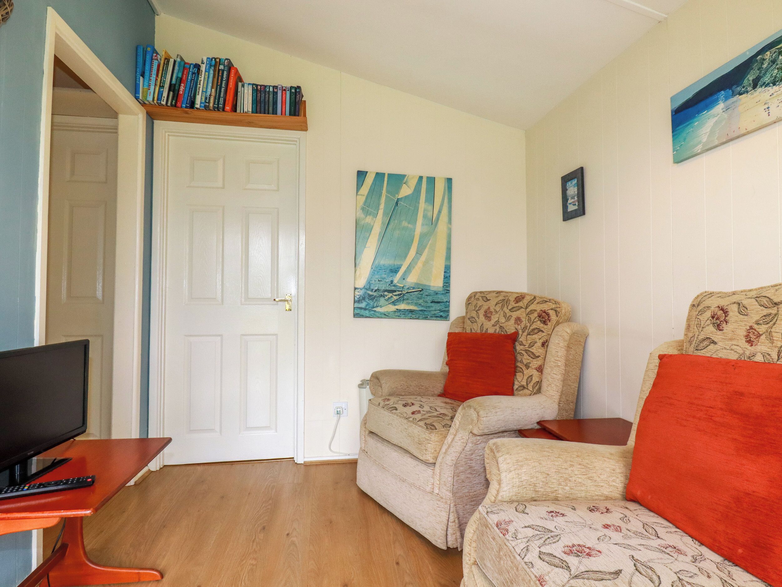 A cozy living room with a television, a bookshelf, a painting of a sailboat, and a floral-patterned sofa.
