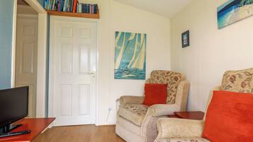 A cozy living room with a television, a bookshelf, a painting of a sailboat, and a floral-patterned sofa.