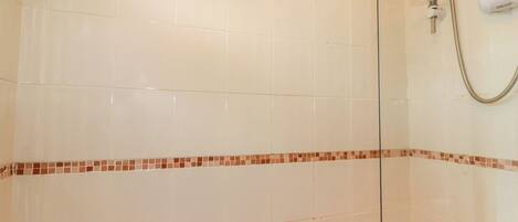A bathroom with white tiles, a shower with a handheld hose, and a bathtub with two faucets.