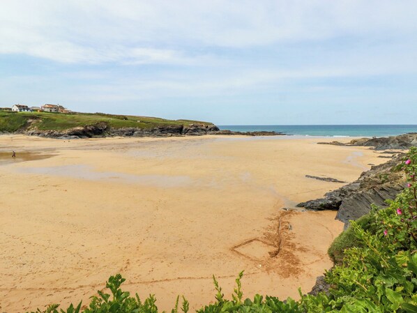 A beach with a rocky shoreline, a clear sky, and a few houses in the background. - Hawker's Cove (Wadebridge)