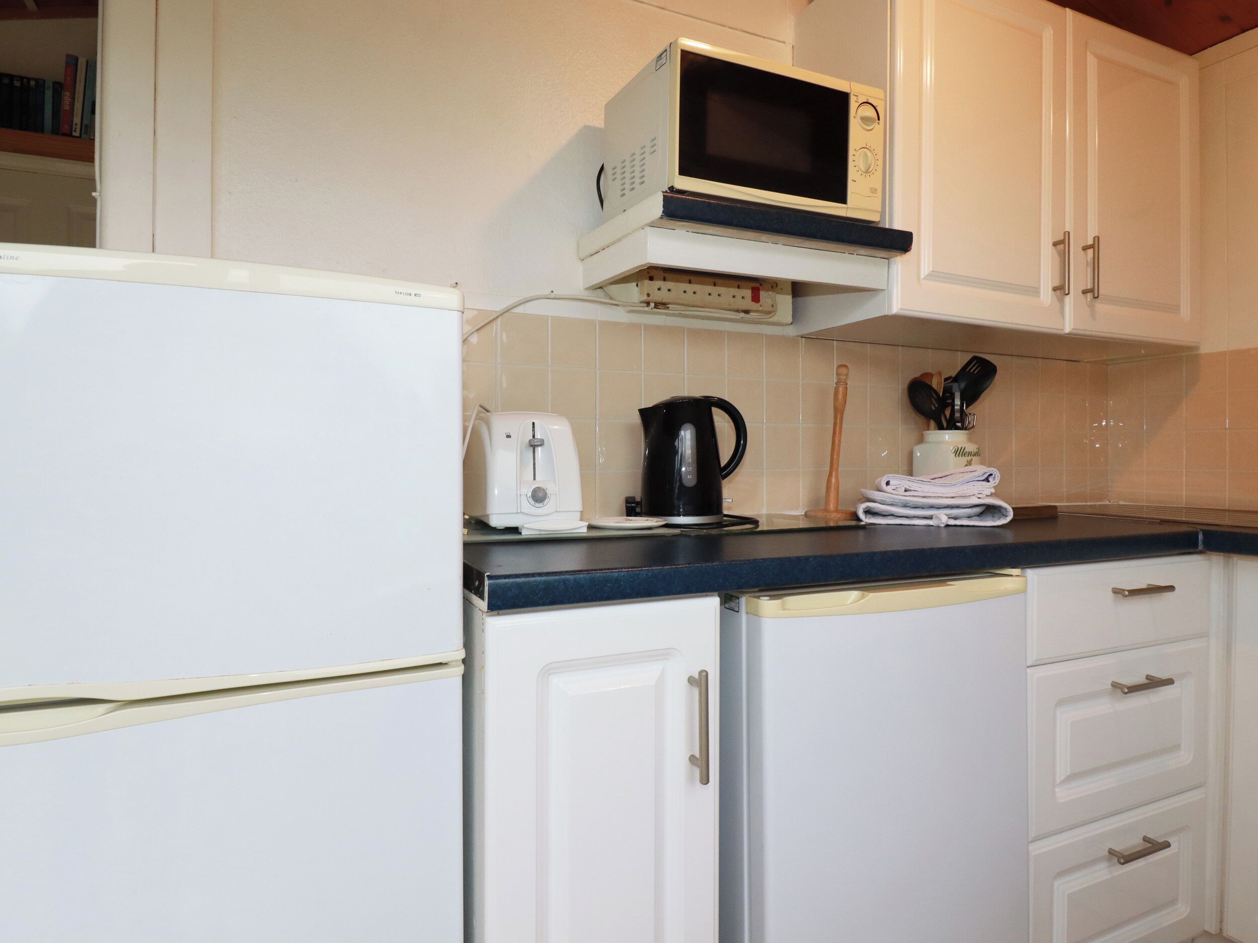 A compact kitchen with a microwave, toaster, kettle, and a coffee maker on the counter.