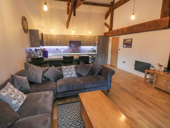 A modern living room with a grey sofa, a wooden coffee table, and a kitchen in the background.