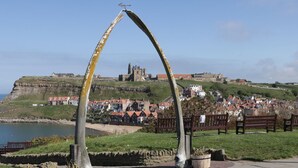 A coastal town with historic buildings, a prominent church, and a cliff overlooking the sea. - Flying Scotsman @ Engine Shed (Whitby)