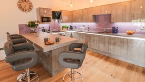 A modern kitchen with a central island, bar stools, wooden cabinets, and a clock on the wall. - Flying Scotsman @ Engine Shed (Whitby)