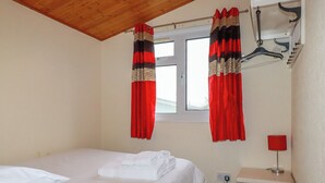 Et soveværelse med seng, natbord, lampe og et vindue med gardiner.