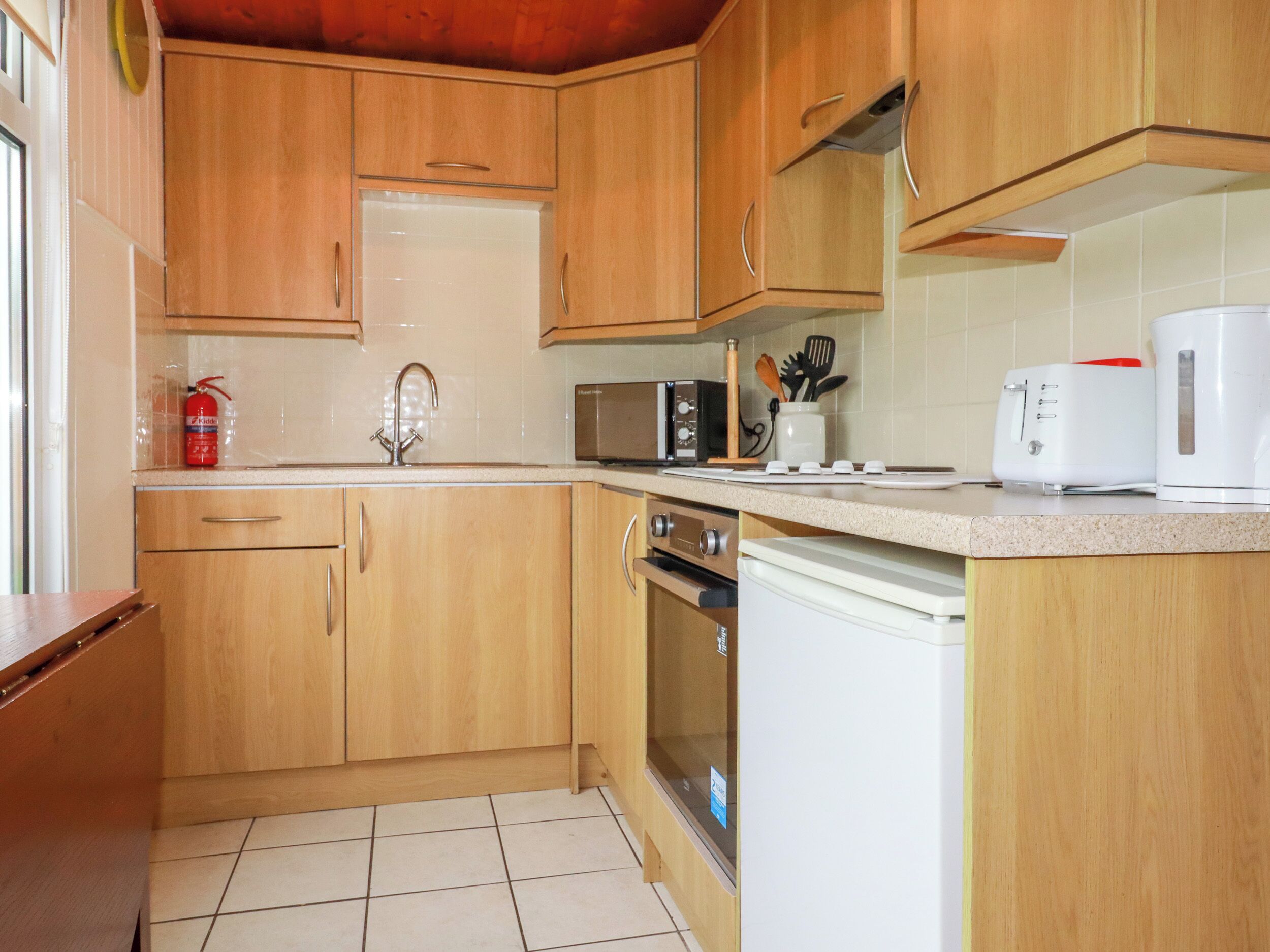 A kitchen with wooden cabinets, a stainless steel sink, a microwave, a toaster, and a dishwasher.