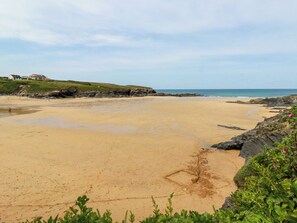 A beach with a rocky shoreline, a grassy hill with a building, and clear skies. - Pepper Cove (Wadebridge)