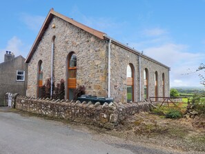 A stone building with a sloped roof, arched windows, and a stone wall foundation. - Ty Capel Pisgah (Pwllheli)