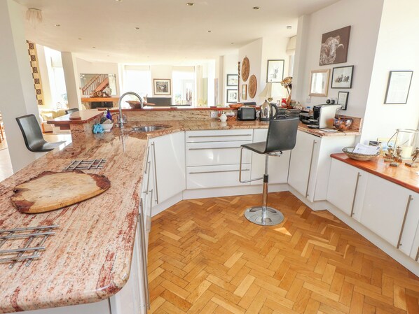 A modern kitchen with a central island, white cabinetry, and a herringbone wood floor. - Ty Capel Pisgah (Pwllheli)