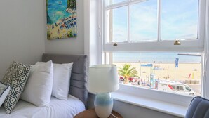 Une chambre d’hôtel avec un lit, une fenêtre donnant sur la plage et un tableau au mur.
