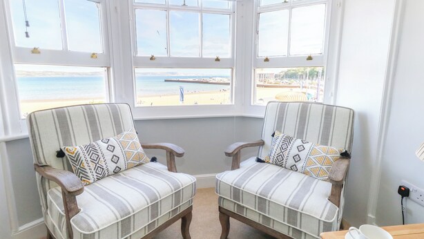 Une pièce avec deux fauteuils à rayures, placés face à une grande baie vitrée donnant sur une plage.