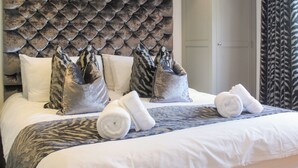 A hotel room with a tufted headboard, a bed with white linens, and a zebra-patterned throw. - Old Police House (Salcombe)