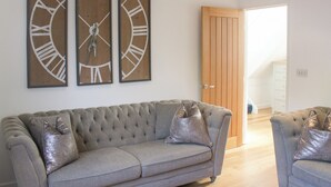 A living room with a grey sofa, two armchairs, and three wall-mounted clocks. - Old Police House (Salcombe)