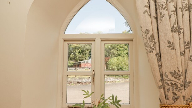 A room with a large arched window, a potted plant on the windowsill, and a curtain with a floral pattern. - Clearbrook Lodge (Carmarthen)