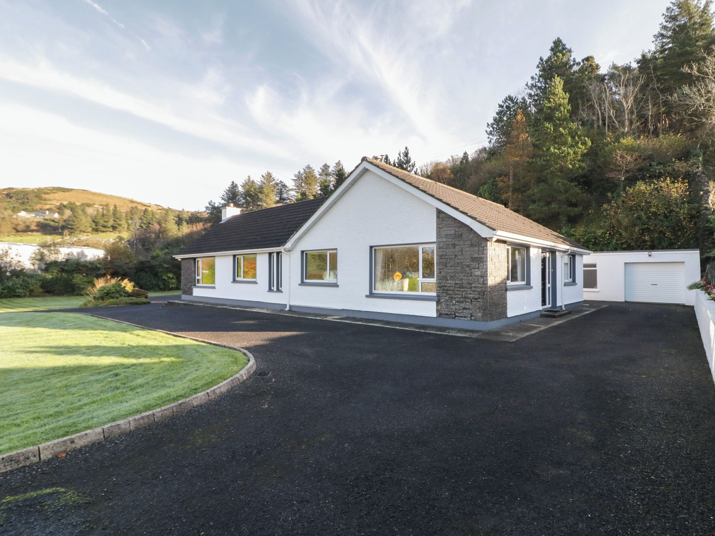 Une maison moderne à deux étages, dotée d’une façade en pierre, de grandes fenêtres et d’un garage.