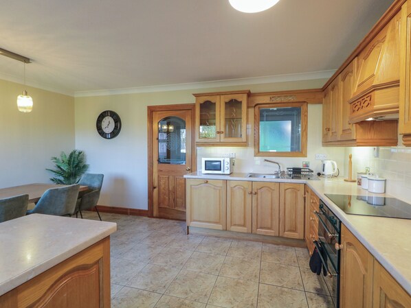 Una cocina con armarios de madera, microondas, lavamanos y comedor con sillas.