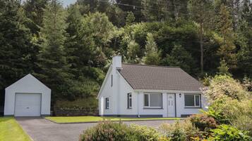 A white house with a tiled roof, a garage, and a well-maintained garden with various plants and flowers.