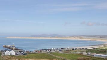 A coastal town with a marina, parked cars, and a clear view of the sea and distant hills.