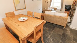 Un coin repas avec une table et des chaises en bois, un canapé en osier et un téléviseur en arrière-plan.