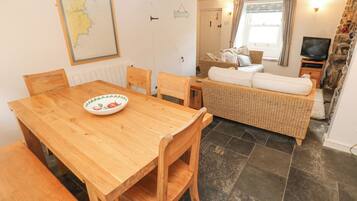 Een eetgedeelte met een houten tafel en stoelen, een rieten bank en een televisie op de achtergrond.
