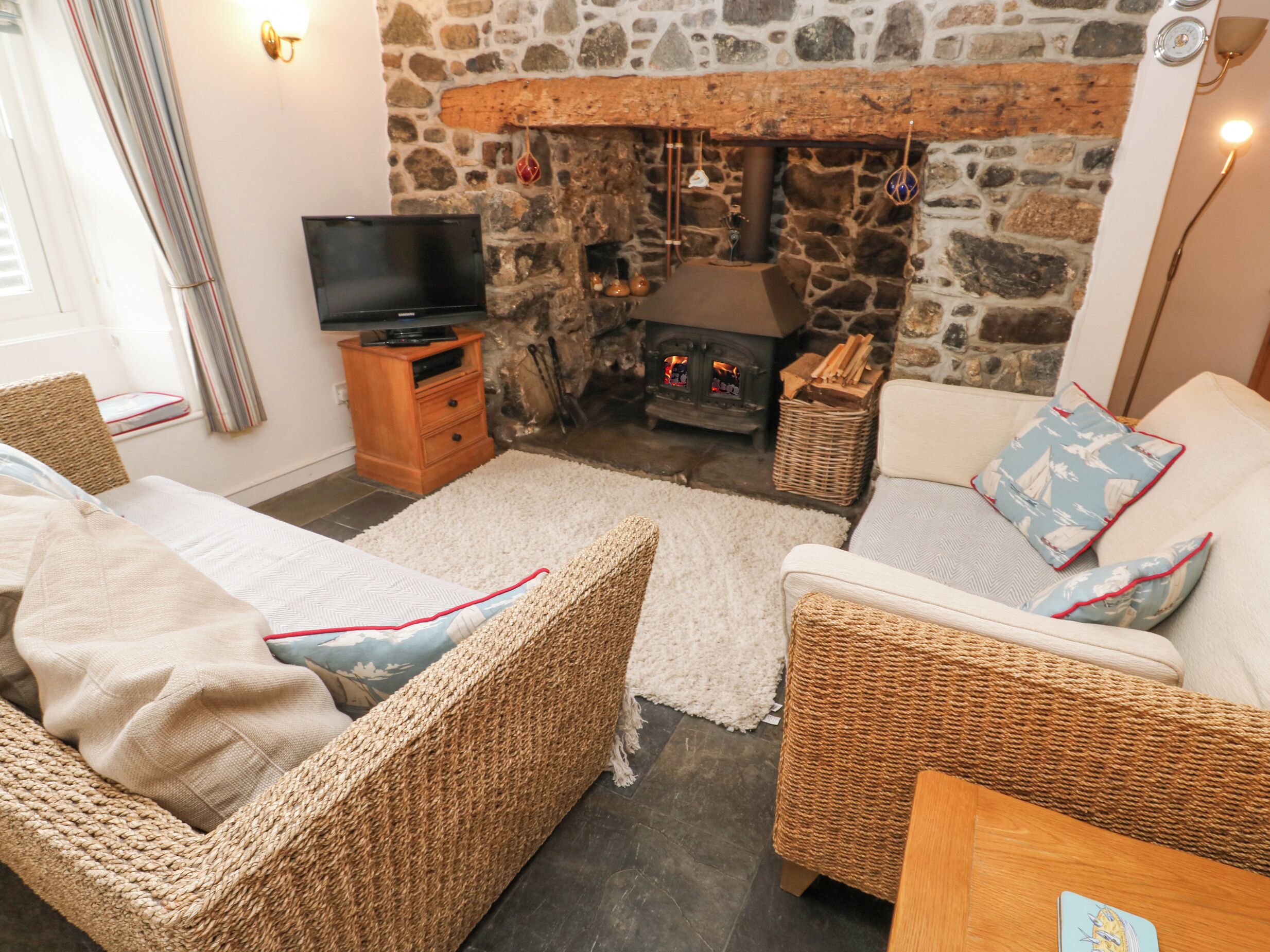 A cozy living room with wicker furniture, a stone fireplace, and a television on a wooden stand.